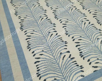 May include: A white rug with a blue and black geometric pattern. The rug has a light blue border with a cream colored stripe.