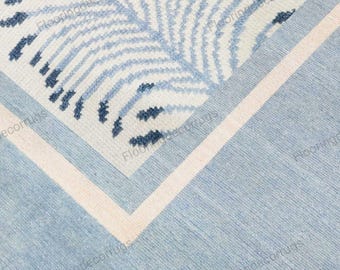 May include: Close-up of a blue and white patterned rug. The rug features a repeating leaf design in shades of blue on a white background. A light blue border surrounds the design, with a thin white stripe. The rug has a textured appearance.