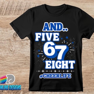 Pode incluir: Camiseta preta com o texto "AND.. FIVE 67 EIGHT #CHEERLIFE" em branco e azul. O design inclui estrelas azuis e uma fonte estilizada. O logotipo Dreamline Designs está no canto inferior esquerdo.