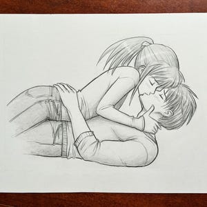 May include: A graphite pencil drawing on white paper depicting two figures in an intimate embrace. One figure with long hair in a ponytail lies partially atop the other, both wearing long-sleeved shirts and jeans, captured in a detailed sketch style.