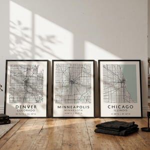 May include: Three framed wall art prints featuring black and white street maps of Denver, Minneapolis, and Chicago. Each print includes the city name, state, and geographic coordinates in a clean, sans-serif font on a light background.