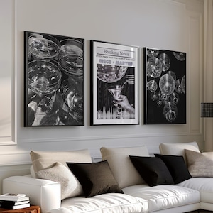 May include: A modern living room with a white sectional sofa, black and beige throw pillows, and three framed black and white art prints. The prints depict cocktail glasses, disco balls, and a martini. A wooden side table and a black coffee table complete the scene.