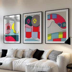 May include: Three framed abstract art prints with black frames hang above a white sectional sofa. The artwork features bold colors and geometric shapes. A black coffee table, a floor lamp, and decorative pillows complete the modern living room setting.