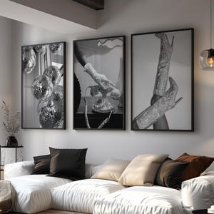Puede incluir: Un salón moderno con un gran sofá blanco, una alfombra estampada y tres impresiones artísticas en blanco y negro enmarcadas. Las impresiones representan bolas de discoteca, un teléfono antiguo y botas de tacón alto. También se ve una lámpara de pie negra y una lámpara colgante.