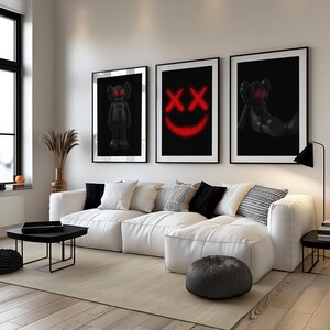 K&ouml;nnte beinhalten: Drei gerahmte Kunstdrucke mit schwarzen Hintergr&uuml;nden. Ein Druck zeigt eine Figur, ein weiterer ein rotes Smiley-Gesicht und der dritte eine Figur in liegender Pose. Die Drucke werden &uuml;ber einem wei&szlig;en Ecksofa in einem modernen Wohnzimmer pr&auml;sentiert.