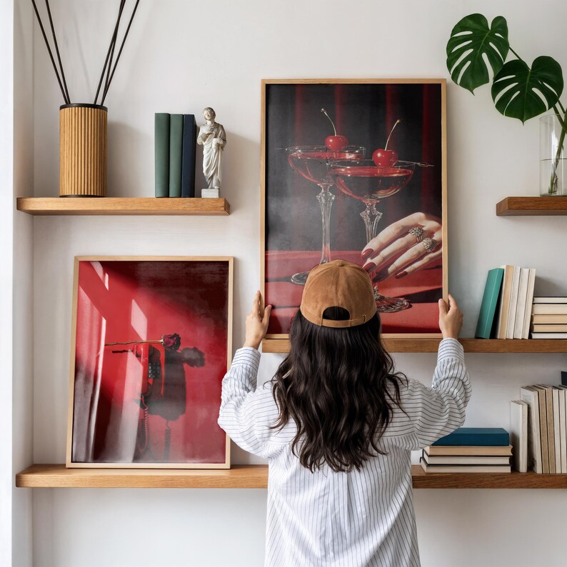 Peut inclure: Deux impressions d'art encadr&eacute;es avec des cadres en bois sont expos&eacute;es sur des &eacute;tag&egrave;res en bois. L'une repr&eacute;sente un cocktail aux cerises, l'autre une image abstraite rouge. Une personne tient l'impression du cocktail.