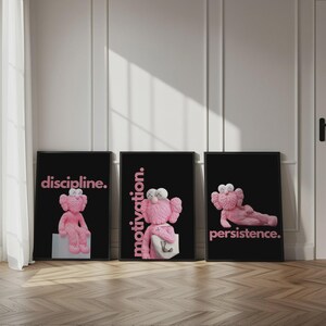 May include: Three framed art prints with black backgrounds and pink text. Each print features a pink cartoon figure. The text on the prints reads "discipline.", "motivation.", and "persistence."