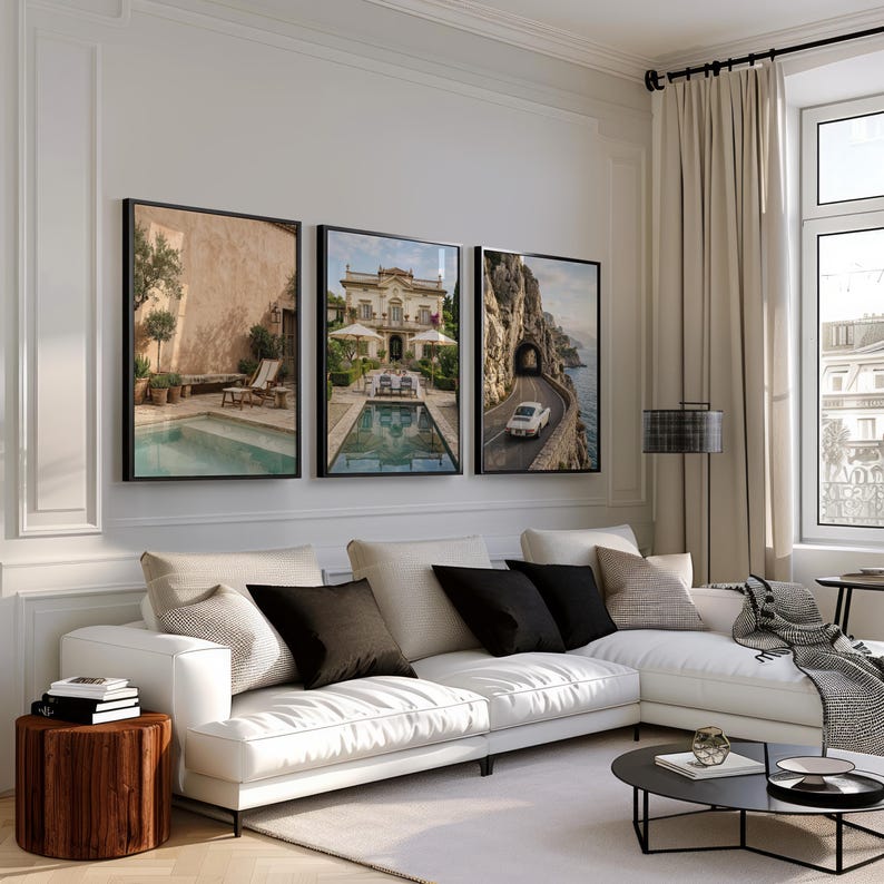 May include: Three framed wall art prints displayed above a white sectional sofa. The left print shows a pool and patio, the center print depicts a villa with a pool, and the right print features a white vintage car driving on a coastal road.