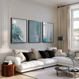 May include: A modern living room featuring a white sectional sofa with black and beige throw pillows. Three framed ocean wave art prints hang above the sofa. A wooden side table and a black coffee table complete the decor.