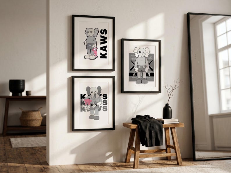 Puede incluir: Tres impresiones art&iacute;sticas enmarcadas con figuras de dibujos animados con ojos en forma de X. Las impresiones est&aacute;n en marcos negros y montadas en una pared blanca. Una impresi&oacute;n tiene la palabra "KAWS" en letras negras grandes. Las otras impresiones tienen las palabras "AIR" y "KAWS".