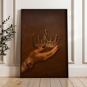 May include: A framed print showing a gold crown with intricate detailing, held in a hand with a gold watch and bracelet. The background is a textured brown, creating a regal aesthetic. The crown is embellished with red gemstones.