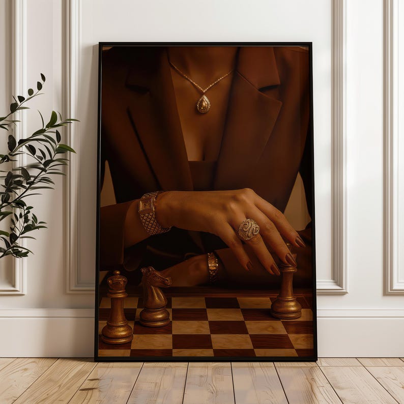 May include: A framed print depicting a chess game. The image focuses on a hand with jewellery, positioned over a chess piece on a chequered board. The scene is set against a brown blazer and a gold pendant necklace.