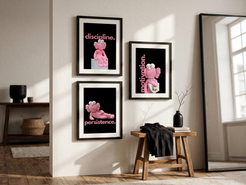 May include: Three framed art prints with black frames hang on a white wall. Each print features a pink cartoon character on a black background with a motivational word in pink: "discipline," "motivation," and "persistence."