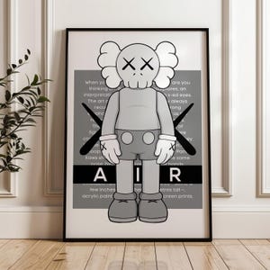 Puede incluir: Un estampado enmarcado que presenta una figura de dibujos animados gris con ojos tachados y guantes. La figura est&aacute; frente a un fondo gris con texto y la palabra "AIR". La obra de arte est&aacute; en un marco negro. Aproximadamente 60 cm de altura.