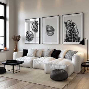 May include: A modern living room featuring a white sectional sofa, a black coffee table, and a neutral rug. Three framed black and white prints hang on the wall: a pool ball, lips, and a leopard. Decorative pillows and a floor lamp complete the space.