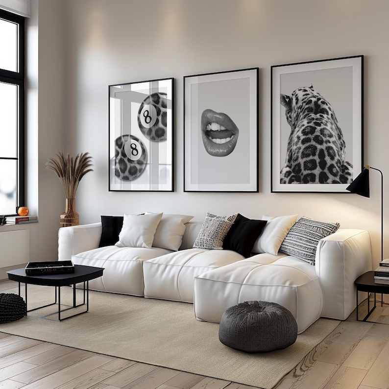 May include: A modern living room featuring a white sectional sofa, a black coffee table, and a neutral rug. Three framed black and white prints hang on the wall: a pool ball, lips, and a leopard. Decorative pillows and a floor lamp complete the space.