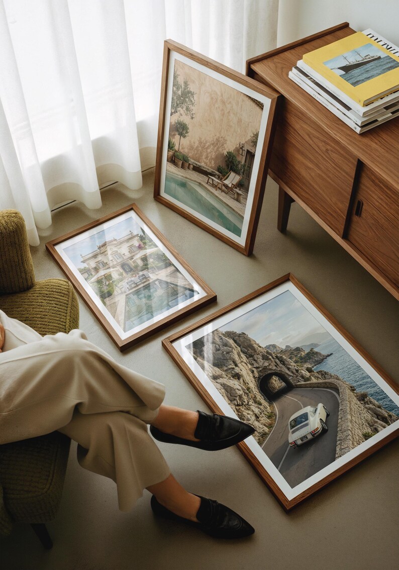 May include: Three rectangular wooden frames containing photographic prints. One print shows a swimming pool, another depicts a large villa with a pool, and the third features a white car driving on a coastal road through a tunnel.