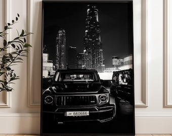 Puede incluir: Una impresión de arte mural enmarcada en blanco y negro que muestra la vista frontal de un SUV negro estacionado frente a un rascacielos por la noche. El vehículo tiene una matrícula con el texto 660666 y escritura árabe en un entorno urbano.