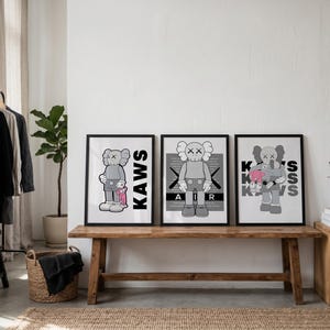 Puede incluir: Tres impresiones art&iacute;sticas enmarcadas con el personaje KAWS en varias poses. Las impresiones est&aacute;n en marcos negros y descansan sobre un banco de madera. El personaje KAWS es gris con huesos cruzados blancos para los ojos y la boca.