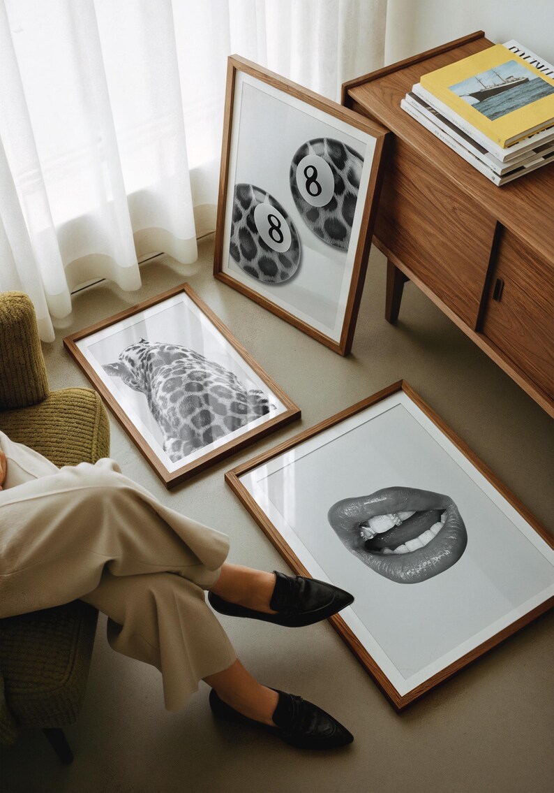 May include: A collection of framed art prints featuring black and white images. The prints include a close-up of a pair of pool balls with the number 8, a giraffe, and a mouth with a diamond. The frames are brown.