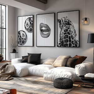 May include: Three framed black and white art prints. One features two pool balls with the number 8, another shows open lips, and the third depicts a leopard's back. The prints hang above a white sectional sofa.
