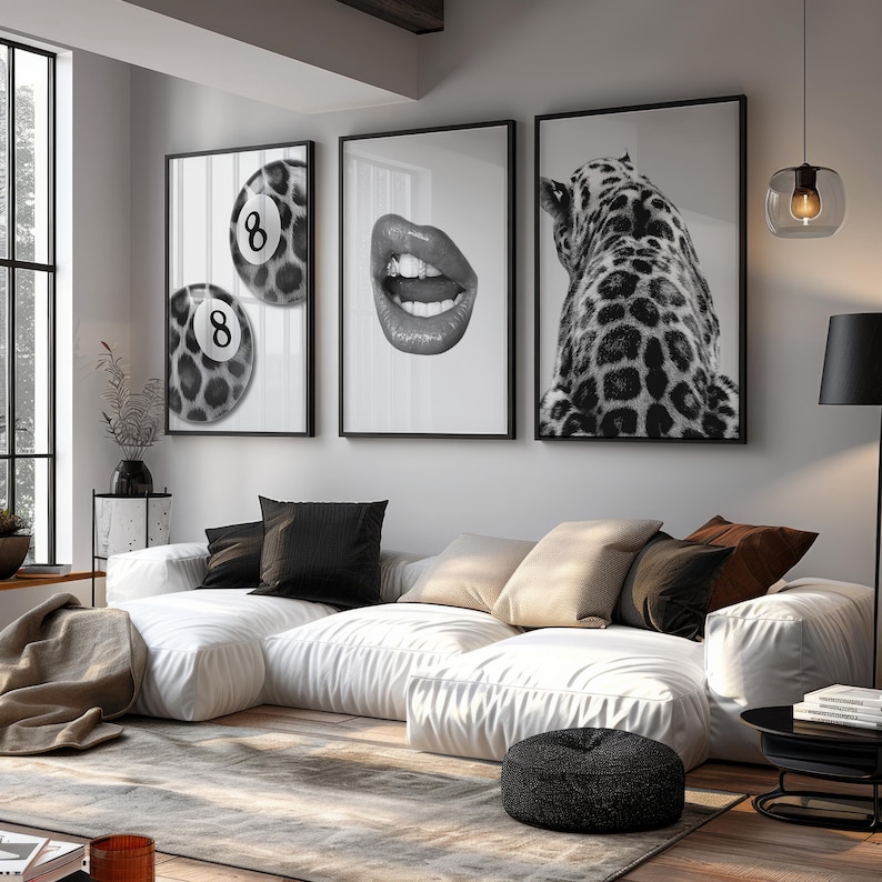 May include: Three framed black and white art prints. One features two pool balls with the number 8, another shows open lips, and the third depicts a leopard's back. The prints hang above a white sectional sofa.