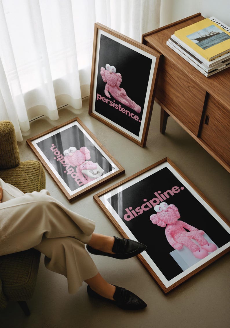 May include: Three framed art prints with a black background and pink text. Each print features a pink cartoon figure in a different pose. The text on the prints reads "persistence", "motivation", and "discipline". The frames are brown.