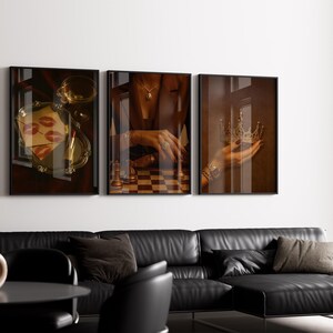 May include: Three framed art prints. The left print shows a tray with lipstick and lip prints. The centre print shows a chessboard. The right print shows a hand holding a crown. A black leather sofa is below the prints.