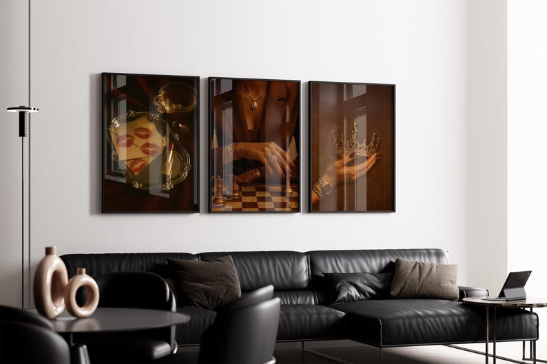 May include: Three framed art prints. The left print shows a tray with lipstick and lip prints. The centre print shows a chessboard. The right print shows a hand holding a crown. A black leather sofa is below the prints.