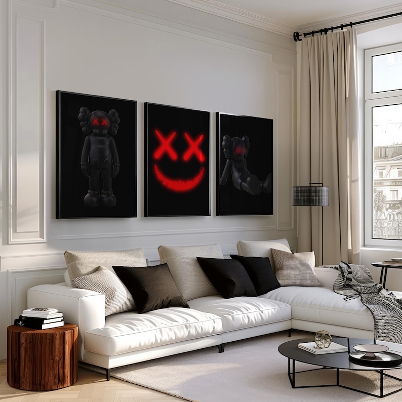 K&ouml;nnte beinhalten: Drei gerahmte schwarze Kunstdrucke mit roten Akzenten. Die Drucke zeigen eine stehende Figur, ein l&auml;chelndes Gesicht und eine sitzende Figur. Die Drucke werden &uuml;ber einem wei&szlig;en Ecksofa mit schwarzen und beigen Kissen angezeigt.