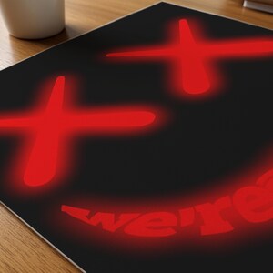K&ouml;nnte beinhalten: Schwarze Oberfl&auml;che mit einem roten Smiley-Gesicht-Design. Das Design umfasst zwei Pluszeichen f&uuml;r die Augen und eine gebogene Linie f&uuml;r den Mund, mit dem Wort "we're" in Rot. Das Design hat einen Leuchteffekt.