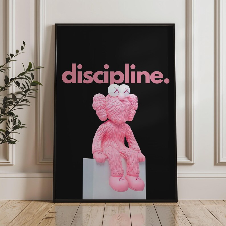 May include: Framed art print featuring a pink, furry character with crossed-out eyes, seated on a gray block against a black background. The word "discipline" is displayed in pink above the character.