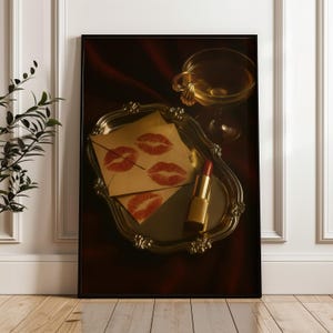 May include: A framed print showing a still life with a vintage silver tray holding lipstick, envelopes with red lip prints, and a champagne glass. The lipstick is gold, and the envelopes are tan.