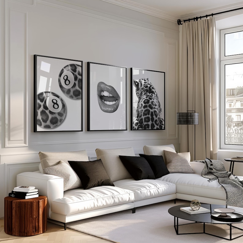 May include: Three framed black and white art prints. One features two pool balls with the number 8, another shows open lips, and the third depicts a leopard's back. The prints hang above a white sectional sofa.