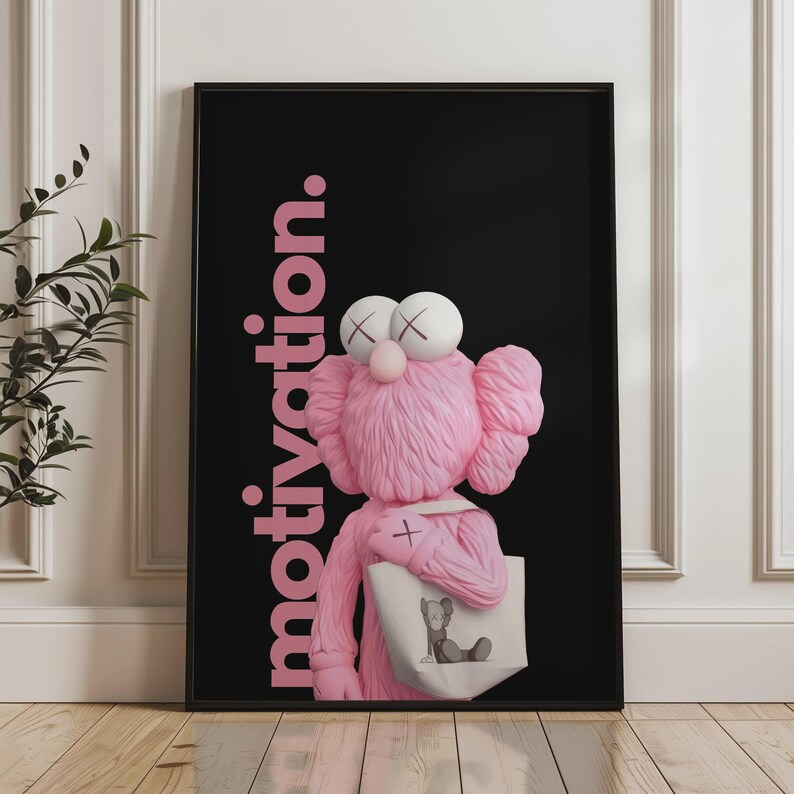 May include: A framed art print featuring a pink cartoon character with white eyes and a cross on its chest, holding a tote bag. The background is black with the word "motivation" in pink.