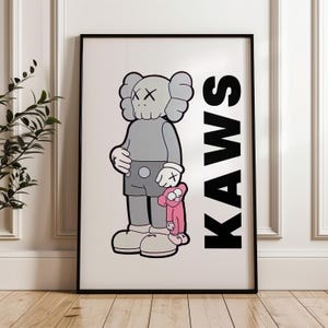 Puede incluir: Impresi&oacute;n art&iacute;stica enmarcada que presenta una figura de dibujos animados gris con ojos tachados, sosteniendo un peque&ntilde;o compa&ntilde;ero rosa. La palabra "KAWS" est&aacute; impresa verticalmente en letras negras en negrita. La obra est&aacute; en un marco negro.
