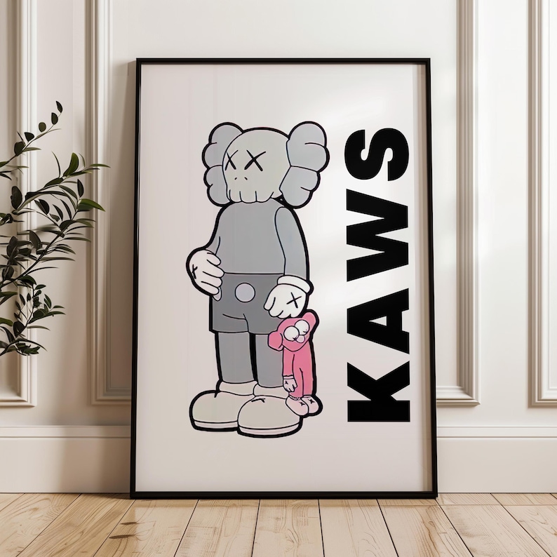 Puede incluir: Impresi&oacute;n art&iacute;stica enmarcada que presenta una figura de dibujos animados gris con ojos tachados, sosteniendo un peque&ntilde;o compa&ntilde;ero rosa. La palabra "KAWS" est&aacute; impresa verticalmente en letras negras en negrita. La obra est&aacute; en un marco negro.