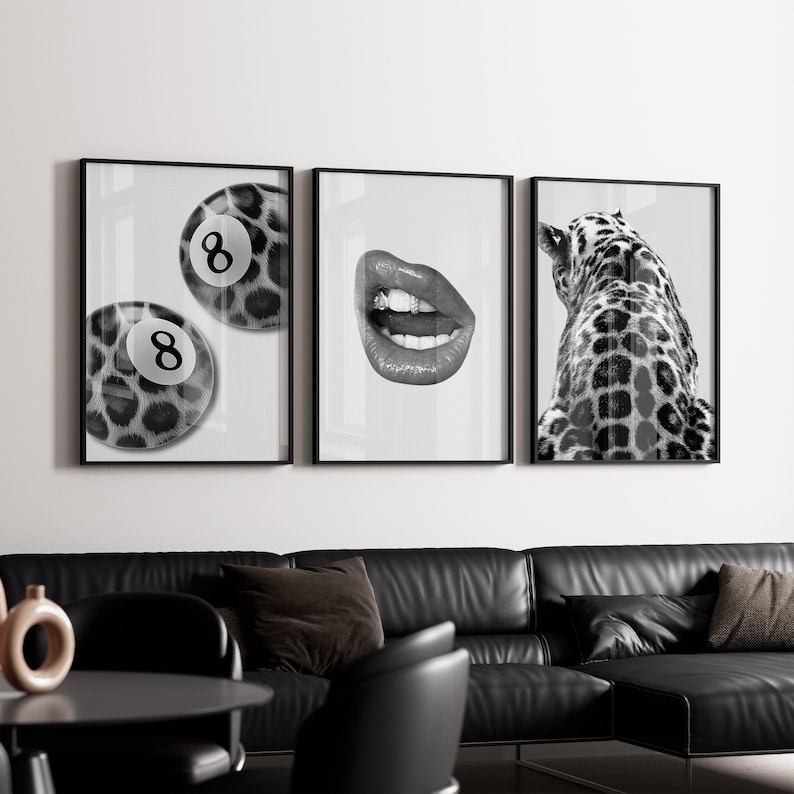 May include: A set of three framed black and white art prints. The prints feature a leopard-print eight ball, a close-up of glossy lips, and the back of a giraffe. The prints are displayed above a black leather sofa.