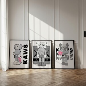 Puede incluir: Tres impresiones art&iacute;sticas enmarcadas que presentan al personaje KAWS en varias poses. Las impresiones est&aacute;n en marcos negros y tienen un fondo blanco. El personaje KAWS est&aacute; representado en tonos grises, con la palabra "KAWS" en letras negras grandes en una impresi&oacute;n.