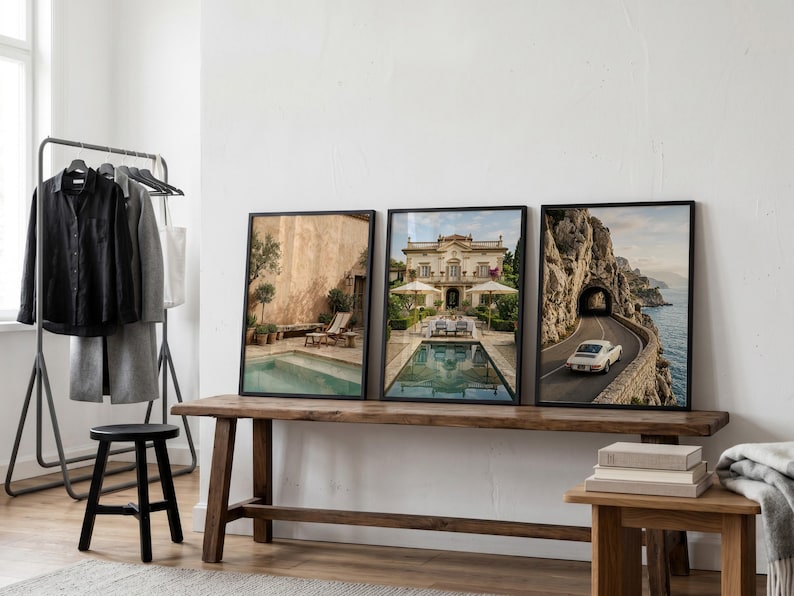 May include: Three framed wall art prints displayed on a wooden bench. The left print shows a pool and patio, the center print depicts a villa with a pool, and the right print features a white car driving on a coastal road through a rock tunnel.