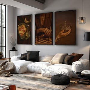 May include: Three framed art prints with luxury themes. One shows a tray with lipstick and kisses, another a hand playing chess, and the third a hand holding a crown. The prints are displayed above a white sectional sofa with black and beige cushions.