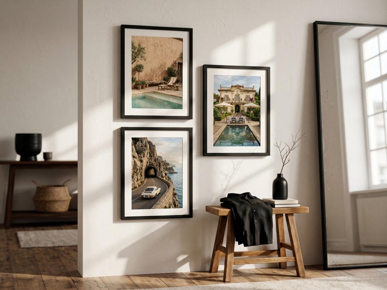 May include: Three framed wall art prints displayed on a white wall. The top left print shows a swimming pool by a building, the bottom left shows a car on a coastal road, and the right print shows a villa with a pool. A wooden bench sits below.