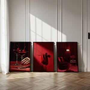 Peut inclure: Trois impressions d'art encadr&eacute;es sur le th&egrave;me du rouge. L'une repr&eacute;sente deux verres &agrave; cocktail avec des cerises, une autre un t&eacute;l&eacute;phone rouge et une rose, et la troisi&egrave;me un fauteuil en velours et une lampe. Les impressions sont affich&eacute;es contre un mur blanc.