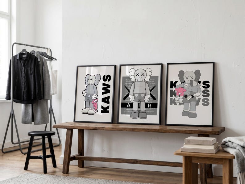 Puede incluir: Tres impresiones art&iacute;sticas enmarcadas con personajes KAWS en escala de grises. Las impresiones se exhiben en un banco de madera. El personaje KAWS se representa en varias poses, con la palabra "KAWS" o "AIR" y "KISS" en las impresiones.