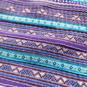 May include: A textile fabric featuring horizontal bands of intricate woven patterns in shades of purple, deep maroon, and bright turquoise. The design includes repeating geometric shapes, small diamond motifs, and thin solid purple stripes.