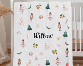 Könnte beinhalten: Weiße Babydecke mit einem sich wiederholenden Muster aus Ballerinas, Nussknackern, Weihnachtsbäumen und anderen Illustrationen zum Thema Feiertage. Der Name "Willow" ist in schwarzer Schrift in der Mitte aufgedruckt.