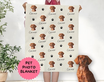 May include: A white pet photo blanket with a repeating pattern of a brown dog's face and the word "Cosmo" printed in black. The blanket is being held by a person.