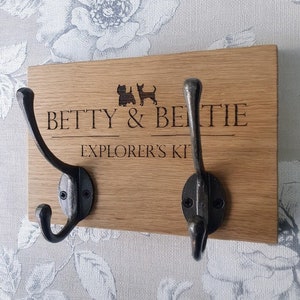 May include: A wooden coat rack with two black metal hooks. The rack is engraved with the text "Betty & Bertie Explorer's Kit" and two small dog silhouettes.