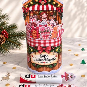 Könnte beinhalten: Eine zylindrische Weihnachts-Geschenkbox mit einer Pop-up-Szene eines Elfen in einem Laden mit Keksen, Zuckerstangen und Kakao. Die Box zeigt den Text "Süße Weihnachtsgrüße" und enthält zwei weiße Röhren mit der Aufschrift "Lasse heißen Kakao" und "du bist bereit für den Weihnachtszauber."