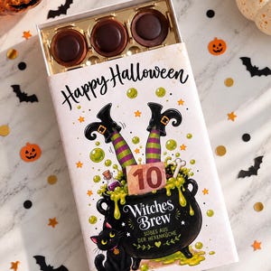 May include: A rectangular box of chocolates featuring a Halloween illustration of a black cauldron with green bubbling liquid, a black cat, and witch legs. The text reads Happy Halloween, 10, Witches Brew, and SÜBES AUS DER HEXENKÜCHE.
